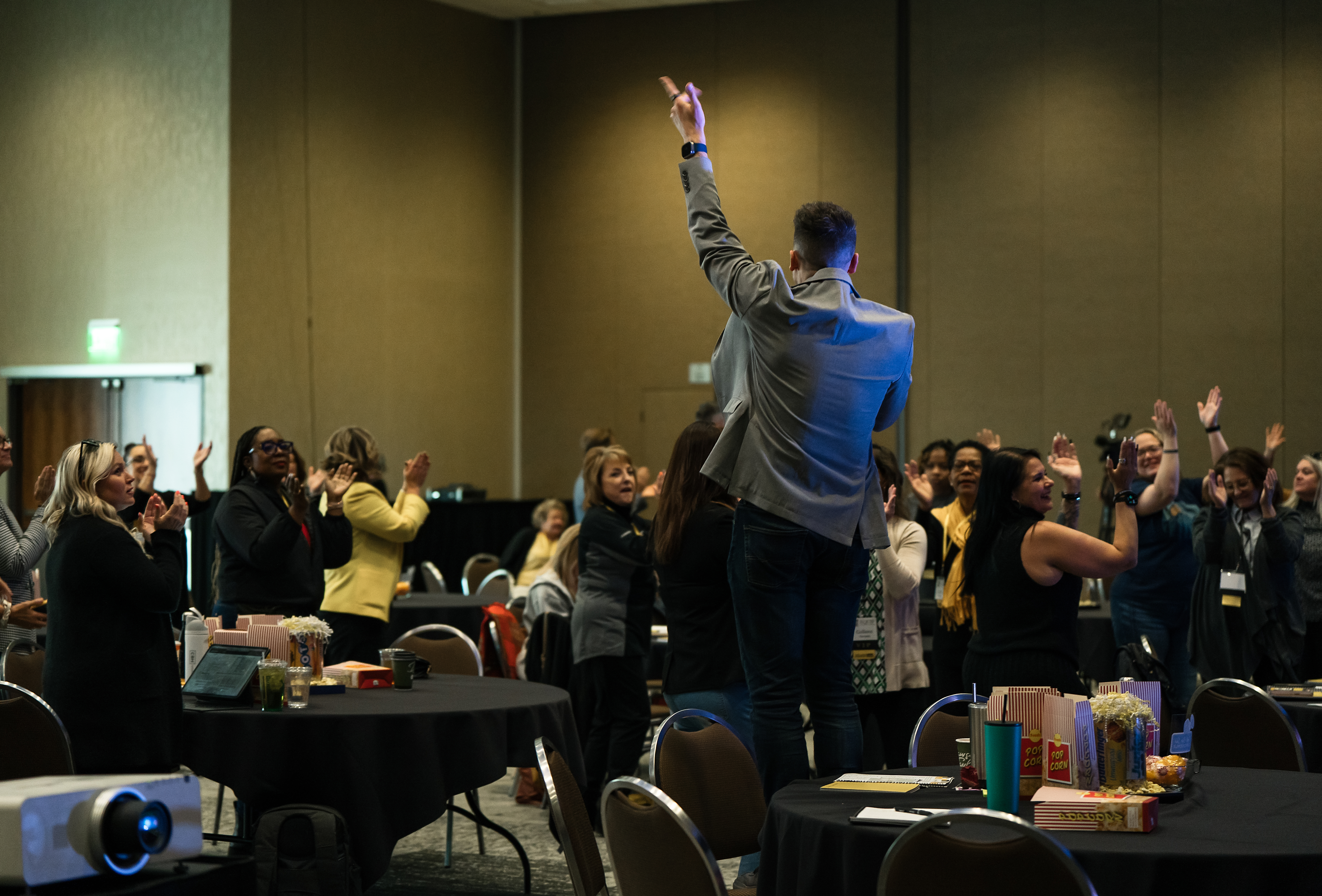 Ross on stage from behind, one arm raised, the entire room's hands in the air