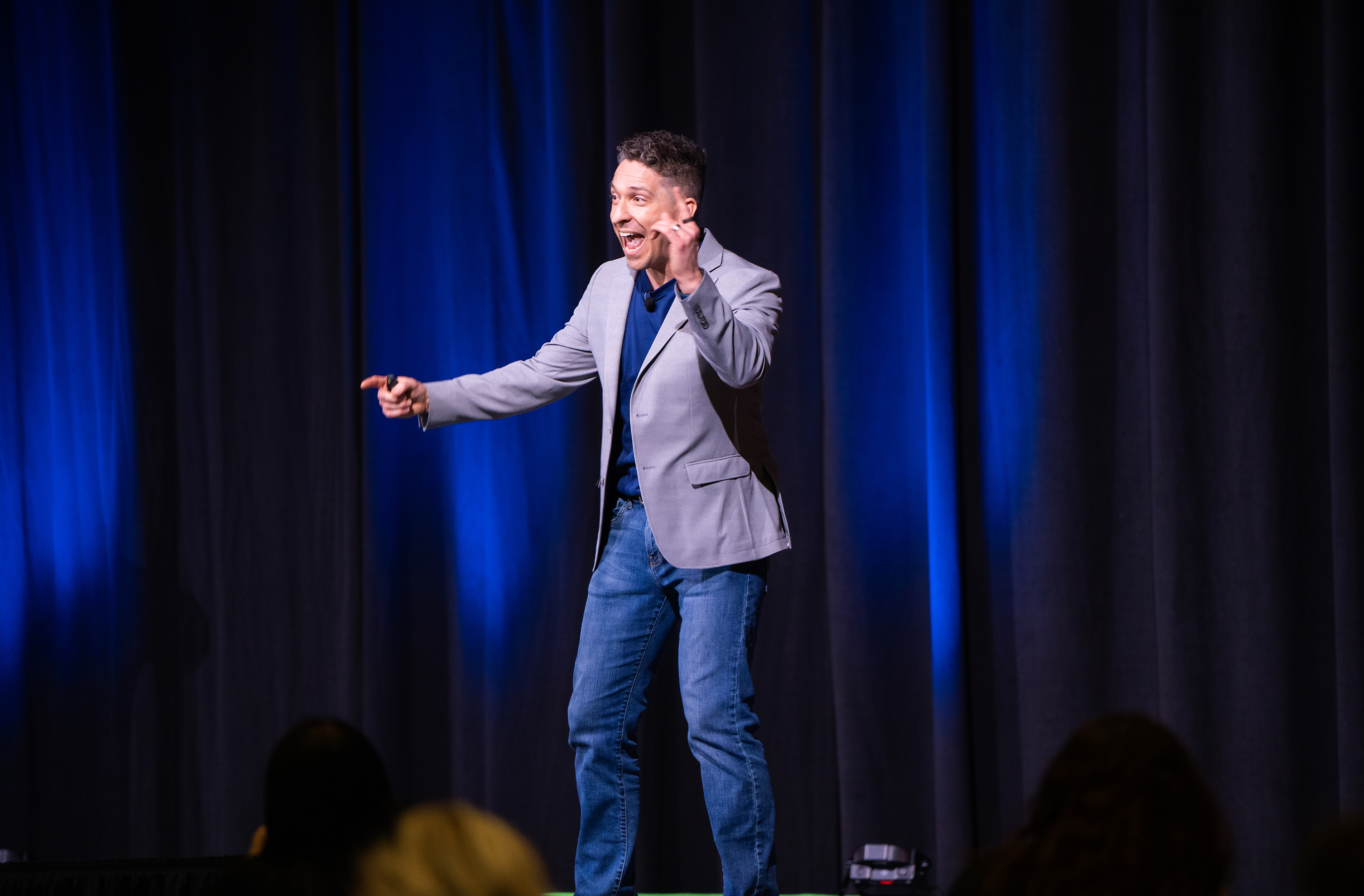 Ross on stage pointing and laughing, audience visible in foreground
